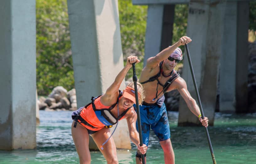 man and woman paddleboarding under a bridge